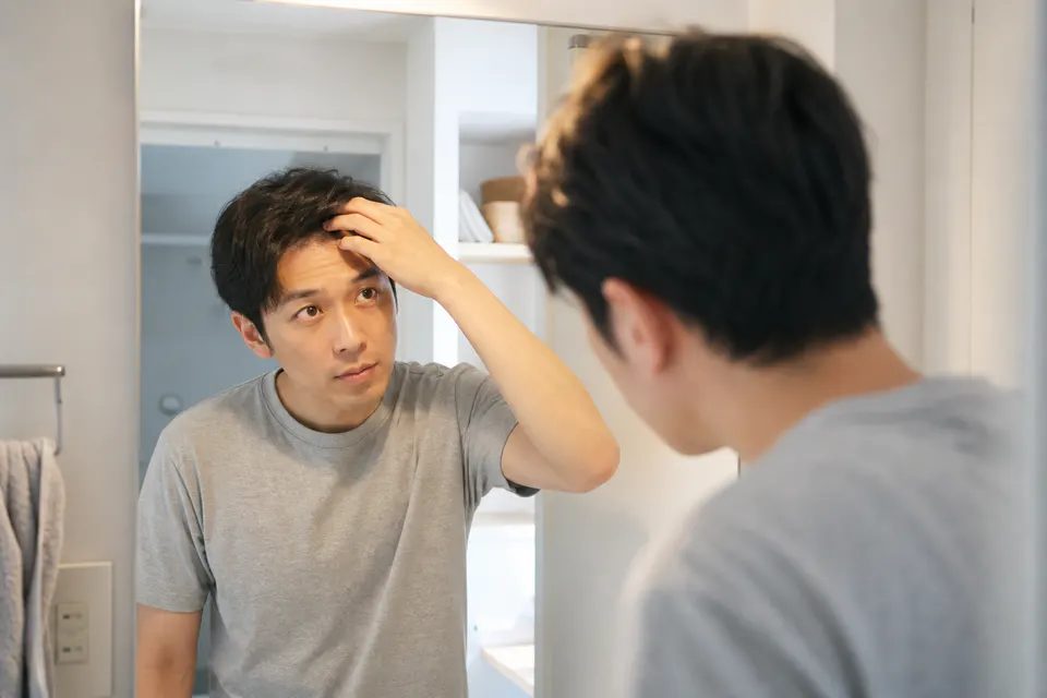 自宅の鏡で生え際を落ち着いて確認する男性