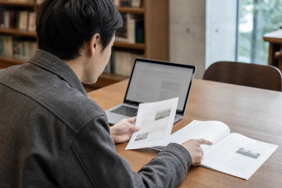 図書館でパソコンと資料の引用元を照合する男性