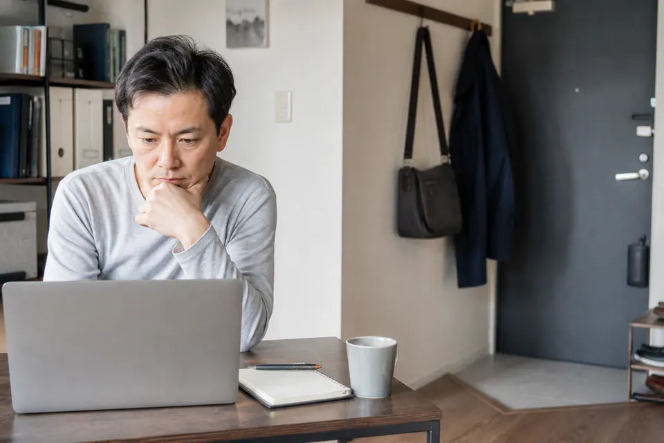 自宅の机でオンライン相談と通院を検討する男性